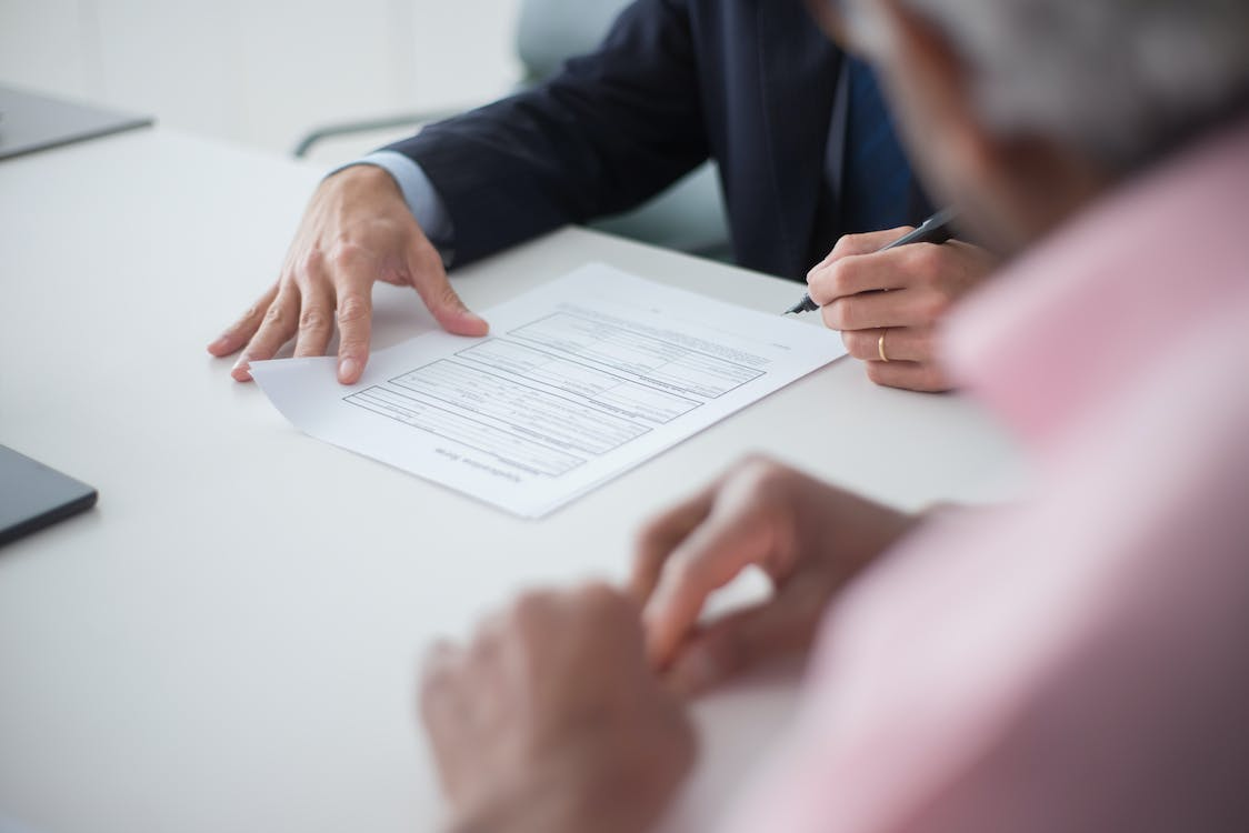 : A man signs a document while sitting next to an insurance agency representative.